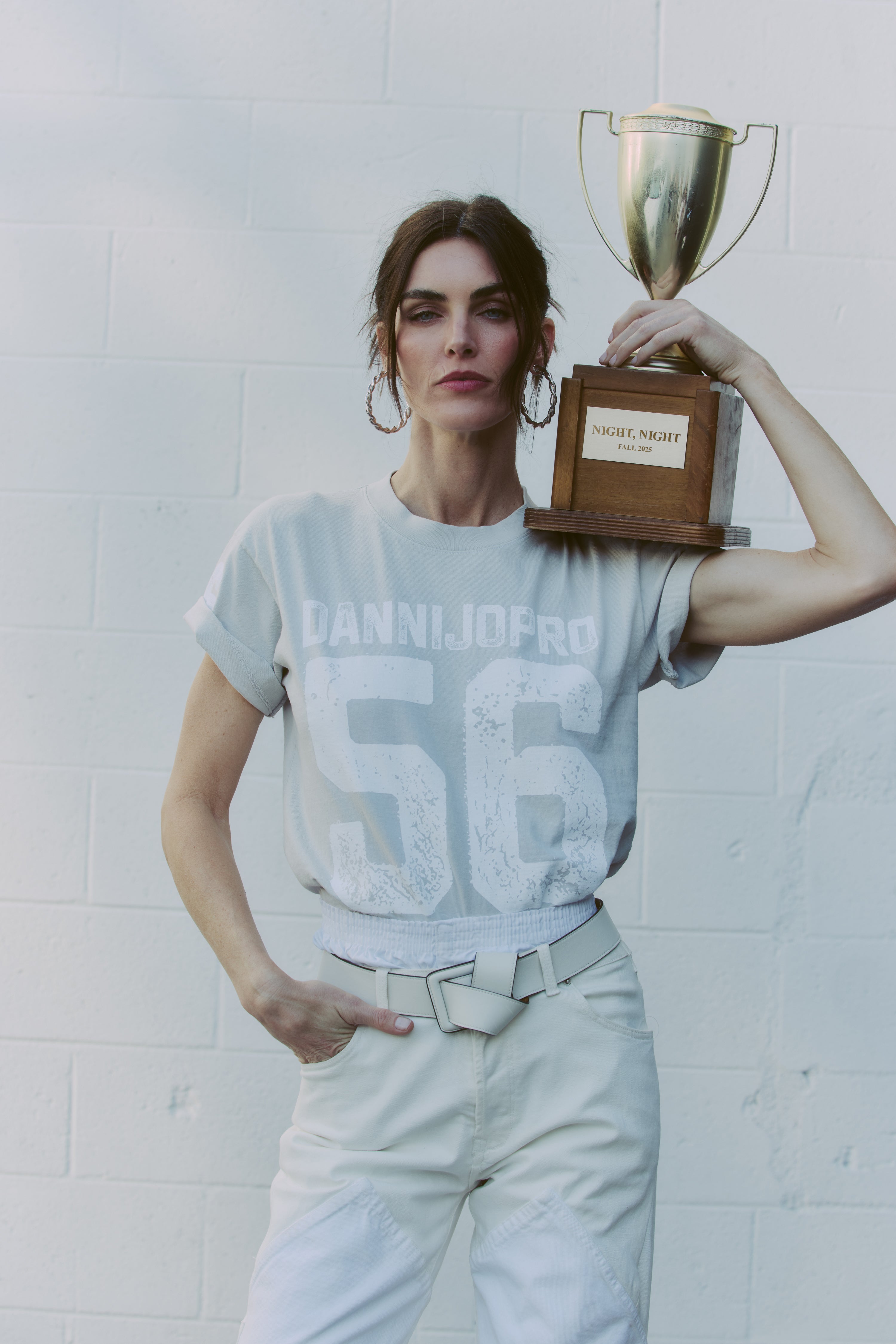 woman holding a trophy against a white wall with a dannijopro t shirt